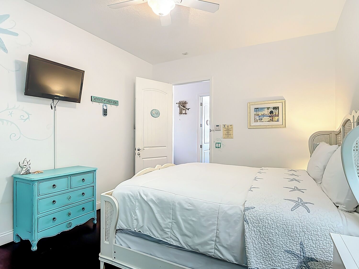 Une chambre à coucher comprenant un lit, une télévision, une commode et une porte donnant sur une autre pièce.