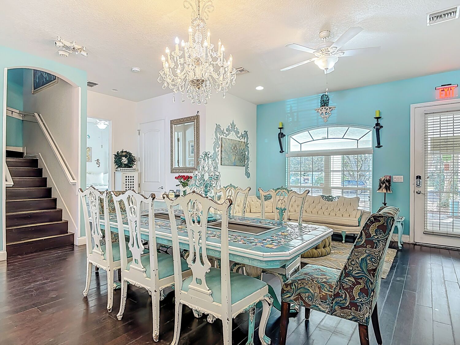 A dining room with a chandelier, a ceiling fan, and a view of the outdoors through a window.