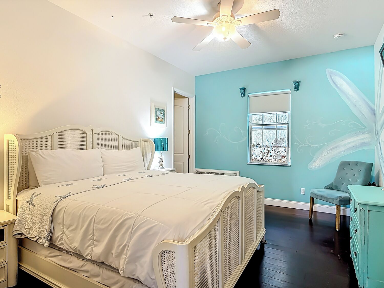 Une chambre à coucher comprenant un lit, un ventilateur de plafond, une fenêtre avec vue, une chaise et une commode.