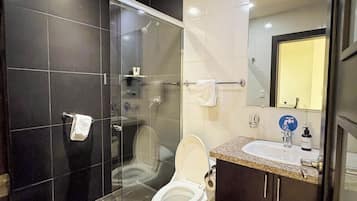 A modern bathroom with a glass-enclosed shower, a toilet, and a sink with a mirror above it.