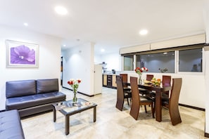 A modern living room with a sofa, a glass coffee table, and a dining area with a wooden table and chairs. - Gaviota Apartments & Suites (Cuenca)