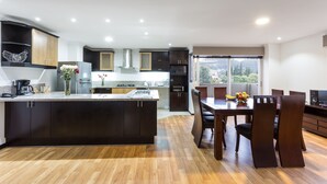 Una cocina moderna con armarios oscuros, una isla central y una zona de comedor con sillas y una mesa de madera.