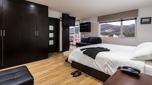 Una habitación de hotel moderna con una cama grande, un televisor y vistas a un paisaje urbano.