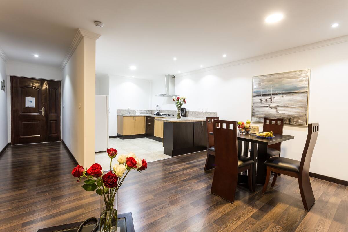 Una cocina moderna con suelo de madera oscura, un comedor con mesa y sillas, y un cuadro en la pared.