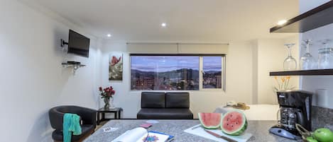 A modern kitchen with a large window, a coffee machine, and a dining area with a black sofa and a book.