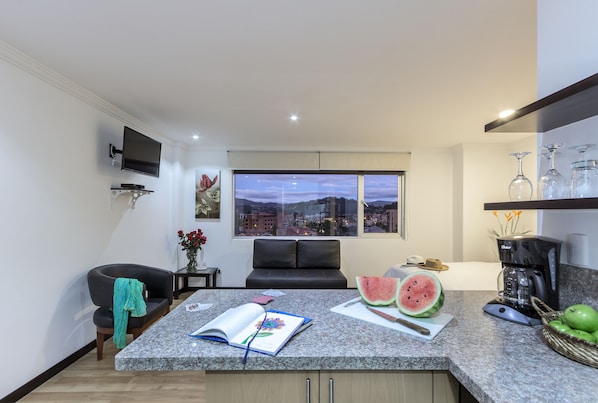 A modern kitchen with a large window, a coffee machine, and a dining area with a black sofa and a book. - Gaviota Apartments & Suites (Cuenca)