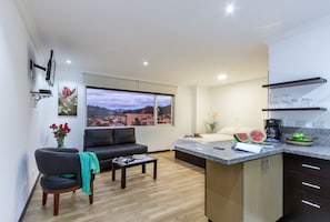 A modern living room with a sofa, a coffee table, and a view of a cityscape through large windows. - Gaviota Apartments & Suites (Cuenca)