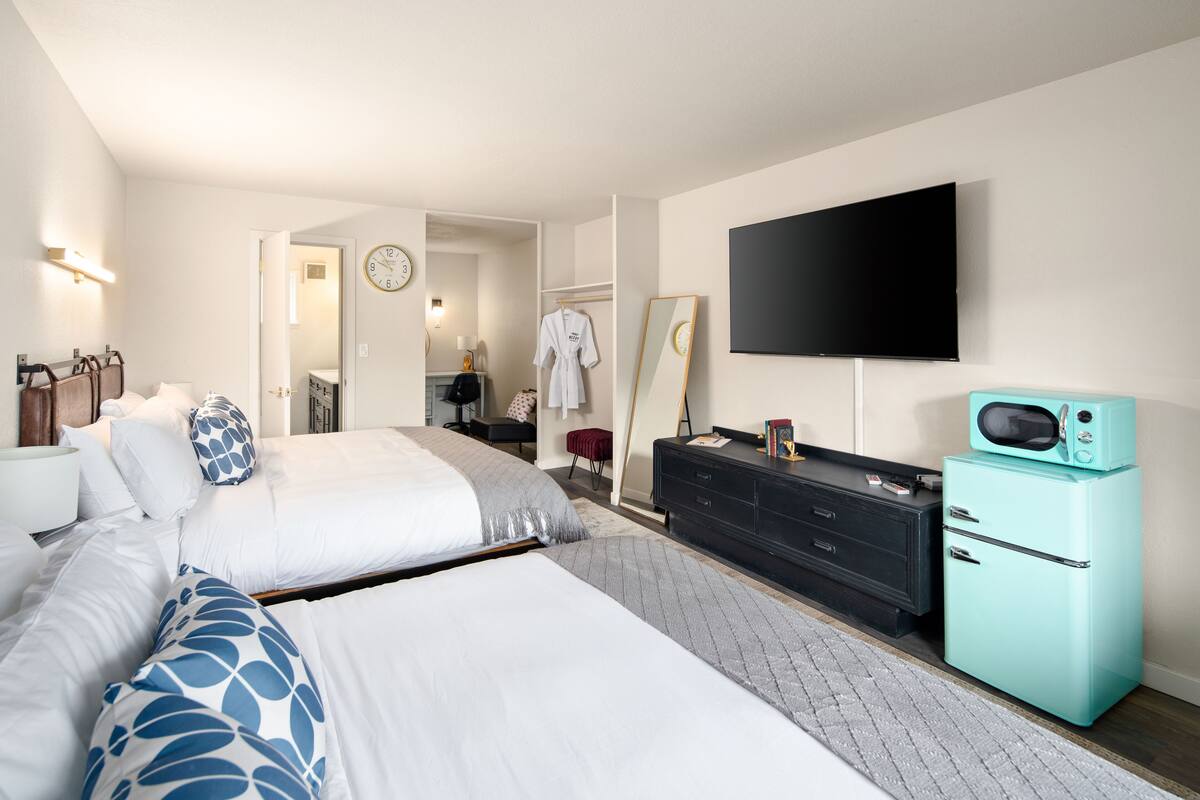 A hotel room with two beds, a TV, a microwave, a dresser, and a mirror.