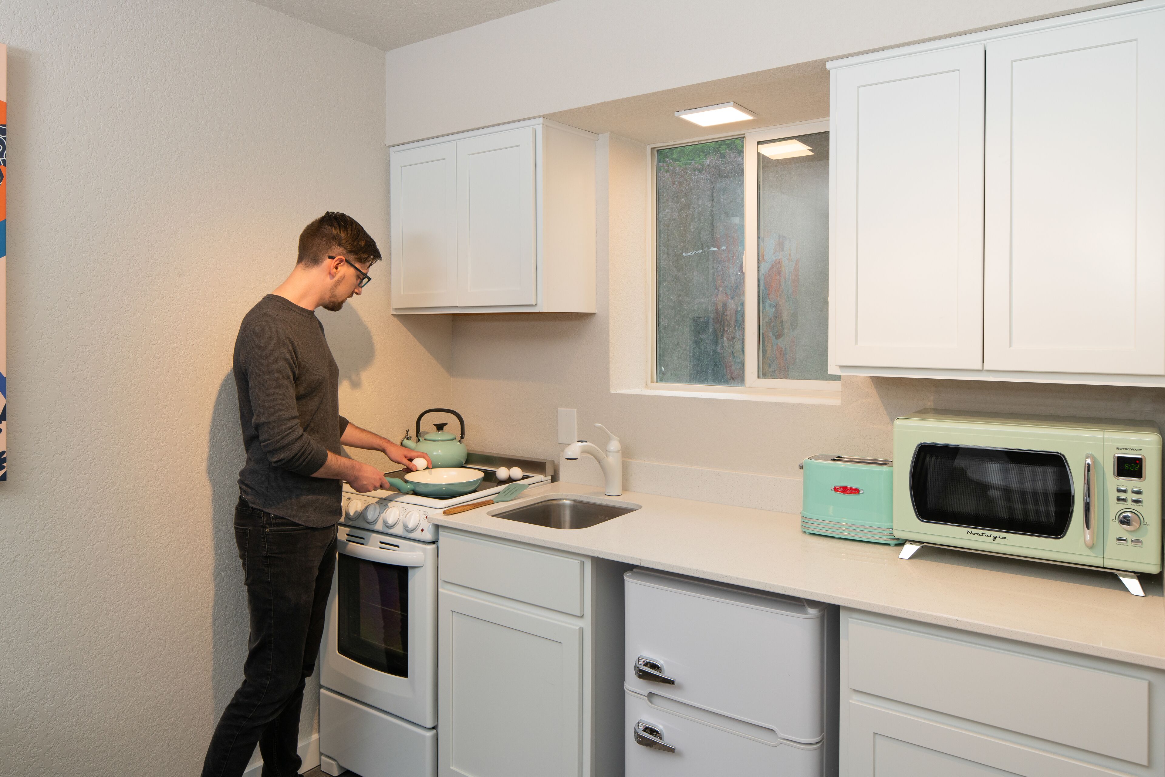 A compact kitchen with white cabinets, a vintage-style microwave, and a small oven.