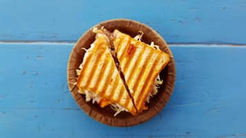 A sandwich cut in half, placed on a brown paper plate, on a blue wooden surface.