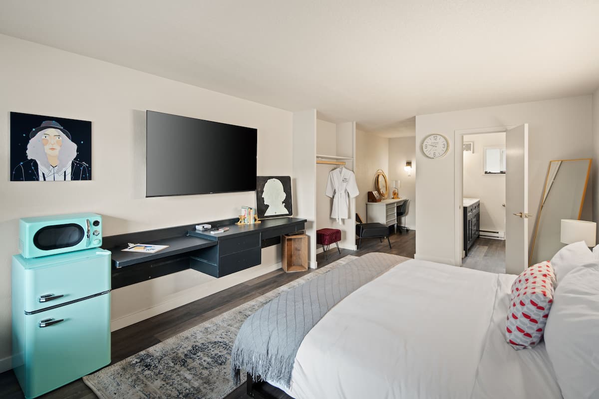 A modern hotel room with a bed, a desk, a television, a microwave, and a wardrobe.