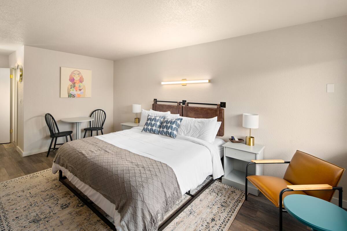 A neatly arranged hotel room with a bed, bedside tables, a chair, a desk, and a small table.