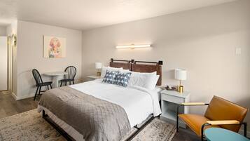 A neatly arranged hotel room with a bed, bedside tables, a chair, a desk, and a small table.
