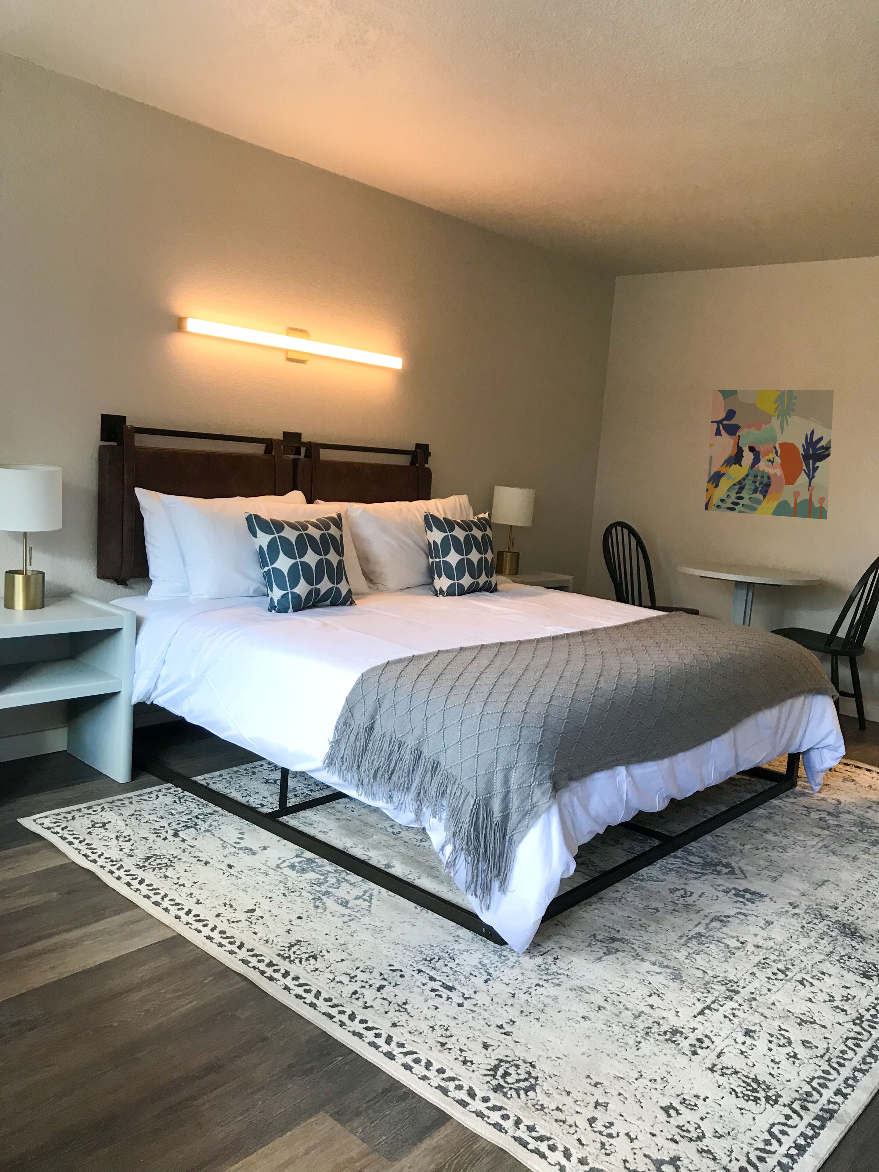 A neatly arranged hotel room with a large bed, bedside lamps, a small table, and a chair.