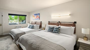 A hotel room with two beds, a large window, a painting, and a bedside table with a lamp.