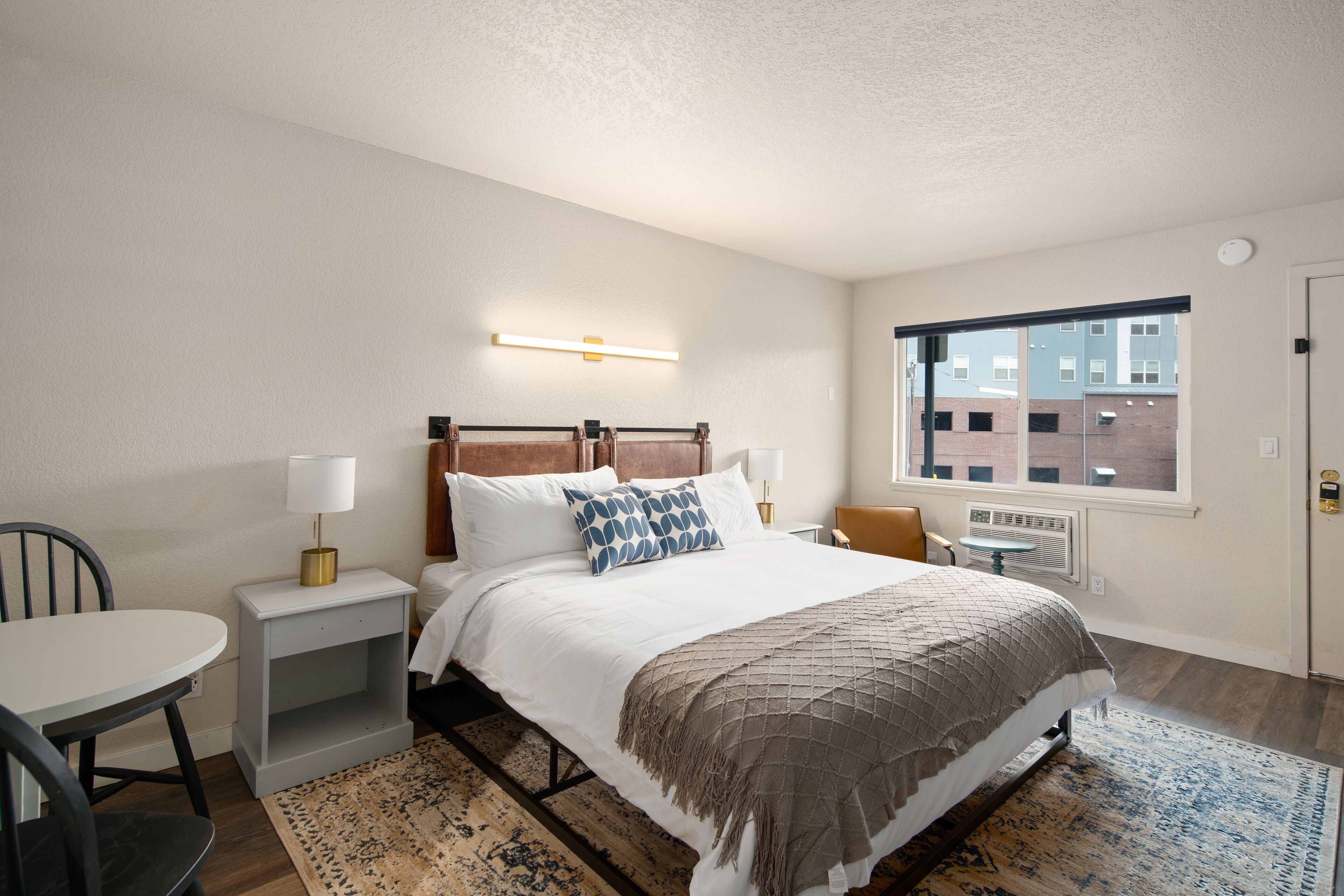 A hotel room with a bed, bedside tables, a chair, a window, and a view of buildings outside.