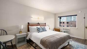 A hotel room with a bed, bedside tables, a chair, a window, and a view of buildings outside.