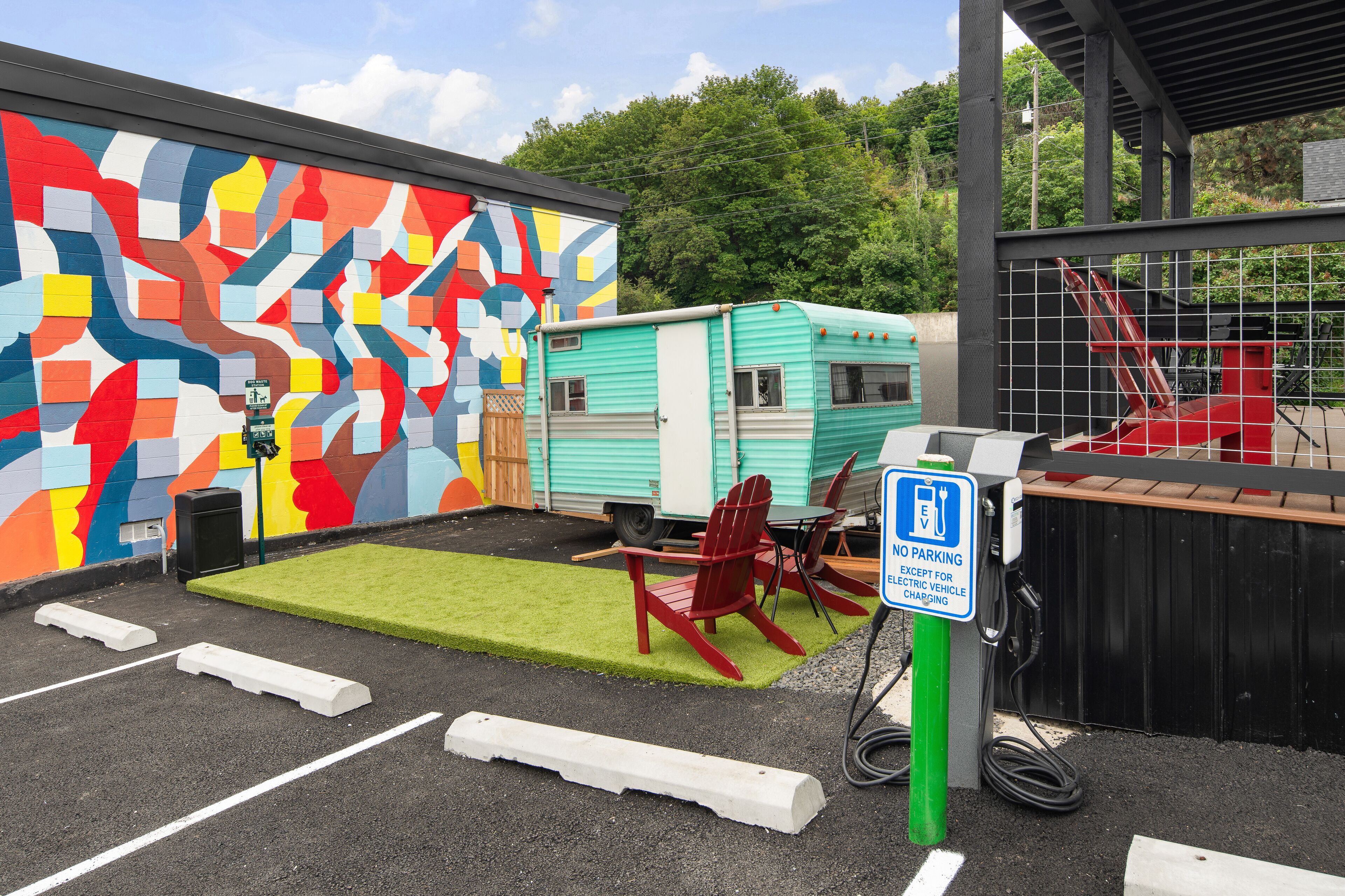 Un estacionamiento con un mural, césped sintético verde, sillas rojas y una caravana.