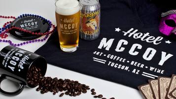 A black mug with coffee beans spilled out, a glass of beer, a can of beer, and a black tray with a hat and beads.