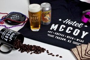 A black mug with coffee beans spilled out, a glass of beer, a can of beer, and a black tray with a hat and beads.
