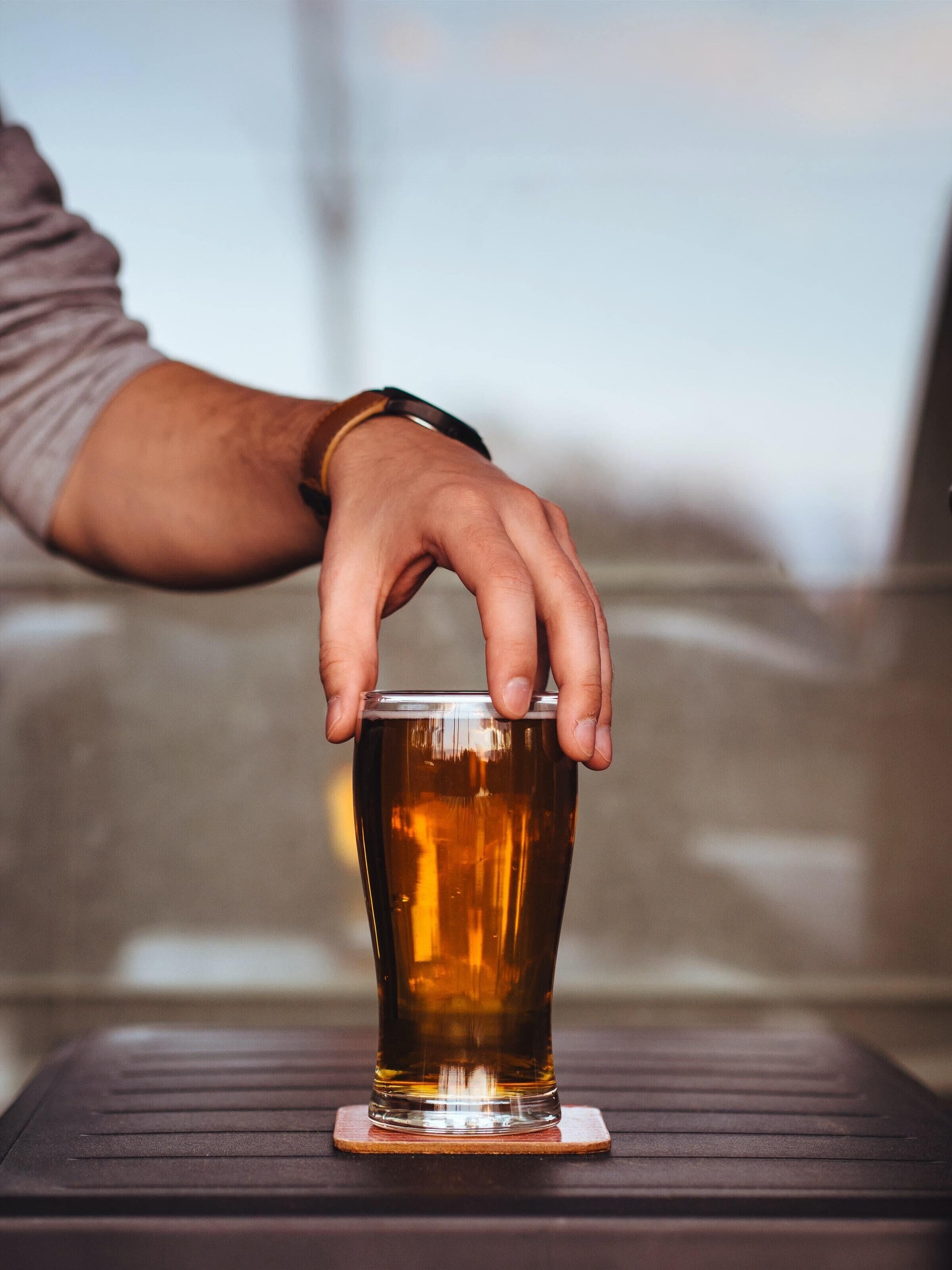 Una mano sosteniendo un vaso con líquido ámbar sobre un posavasos.