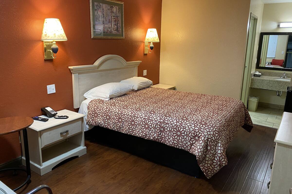 A hotel room with a bed, bedside lamps, a nightstand, a desk, and a mirror.