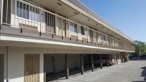 A building with a flat roof, a balcony with metal railings, and a parking area with cars. - Bayview Motel (Emeryville)