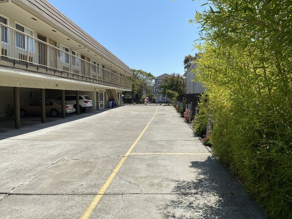 A parking area with cars, a building with a balcony, and greenery.