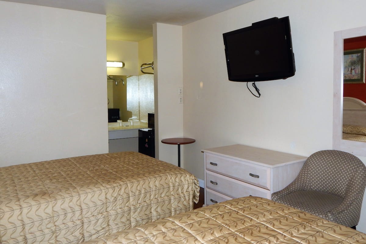 A hotel room with two beds, a TV mounted on the wall, a small table, and a chair.