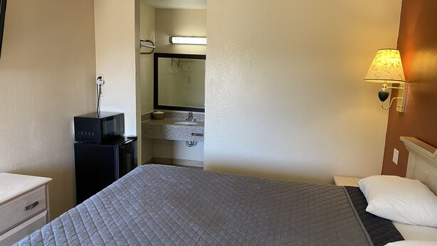 A hotel room with a bed, a desk with a microwave, a sink, and a mirror. - Bayview Motel (Emeryville)