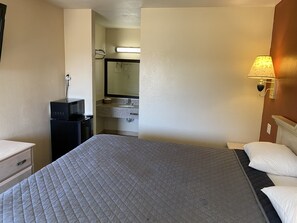 A hotel room with a bed, a desk with a microwave, a sink, and a mirror.