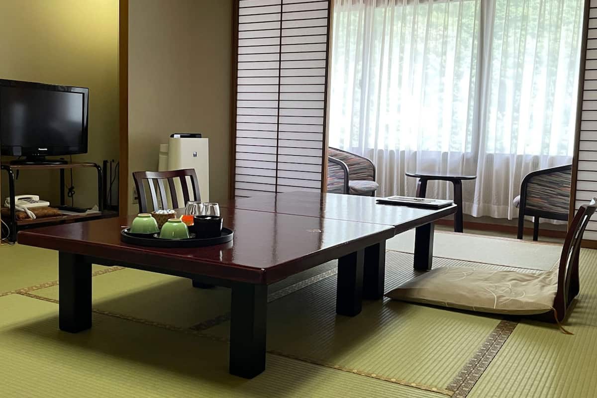 Una habitación japonesa tradicional con suelo de tatami, una mesa baja con un juego de té, un televisor y un calentador.
