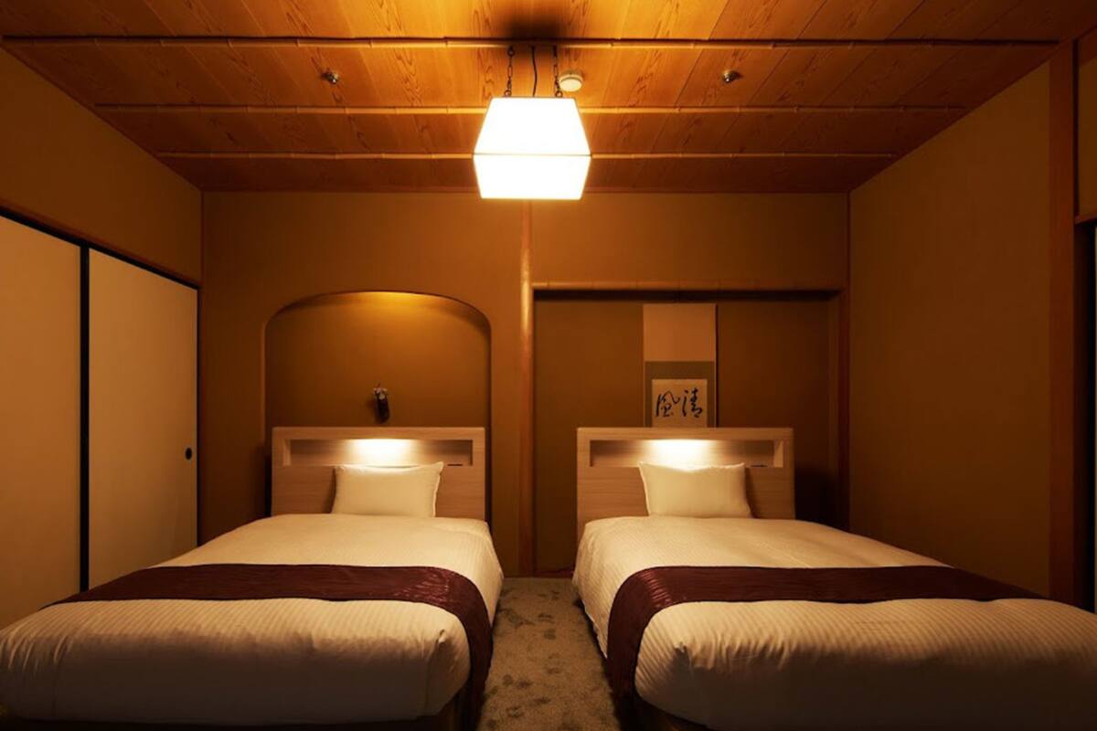 Habitación de hotel con dos camas, techo de madera y una lámpara.