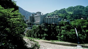 Un hôtel à plusieurs étages, entouré d’une végétation luxuriante et bordé par une rivière.
