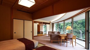 Une chambre d’hôtel avec deux lits, un coin repas et de grandes fenêtres donnant sur l’extérieur.