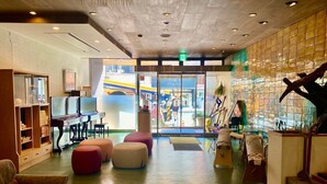 A lobby with a piano, seating areas, a reception desk, and a glass wall with a view of the outside. - Oka Hotel (Kanazawa)