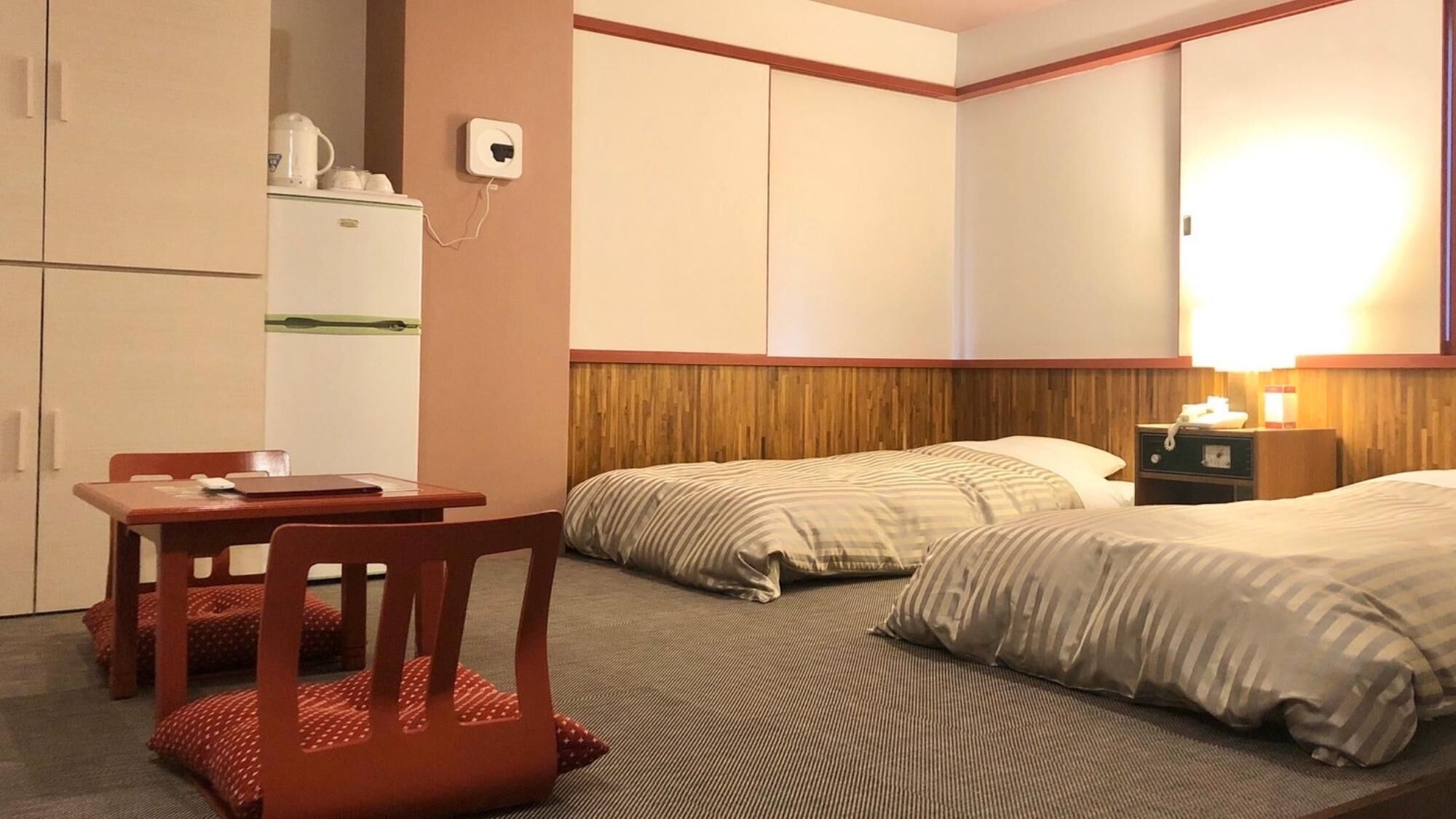 Una habitación de hotel con cama, escritorio, silla, refrigerador y mesita de noche con lámpara.