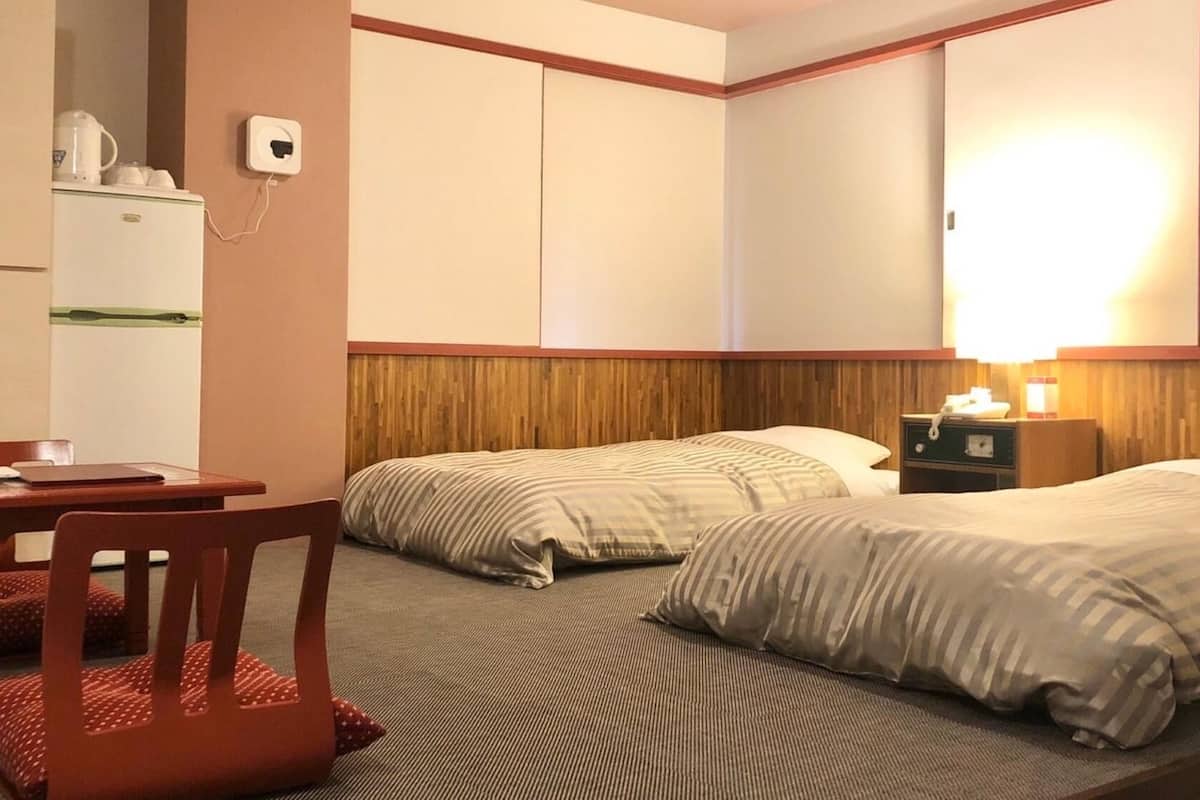 Una habitación de hotel con cama, escritorio, silla, refrigerador y mesita de noche con lámpara.