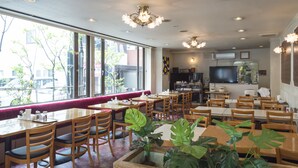 A restaurant with wooden tables and chairs, large windows, and a kitchen area visible through the glass. - Oka Hotel (Kanazawa)