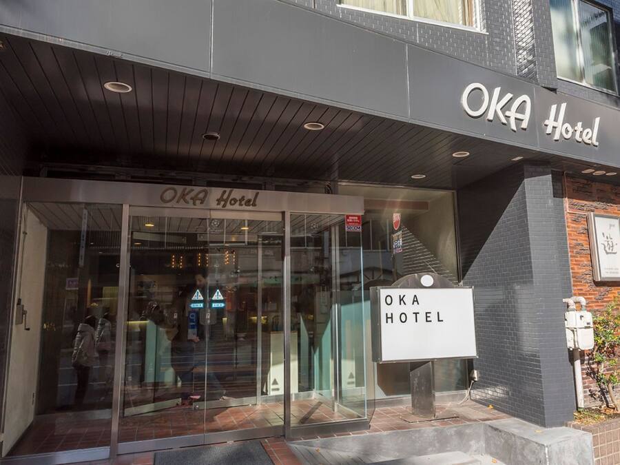 The exterior of the OKA Hotel with a modern facade, glass entrance, and signage.