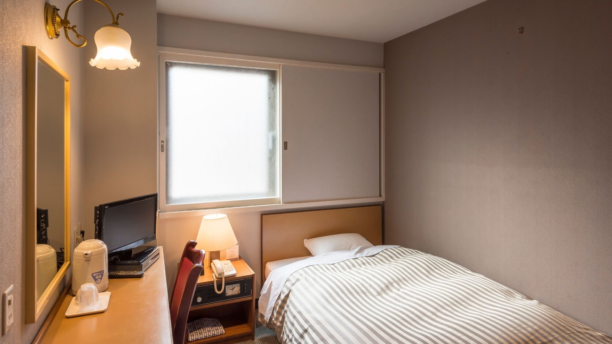 Habitación de hotel con cama, escritorio con teléfono, lámpara, espejo y ventana con persianas.