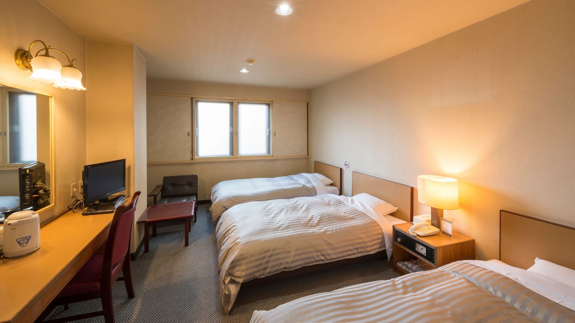 Habitación de hotel con dos camas, un escritorio con computadora, una silla, una lámpara de escritorio y una mesita de noche con teléfono.