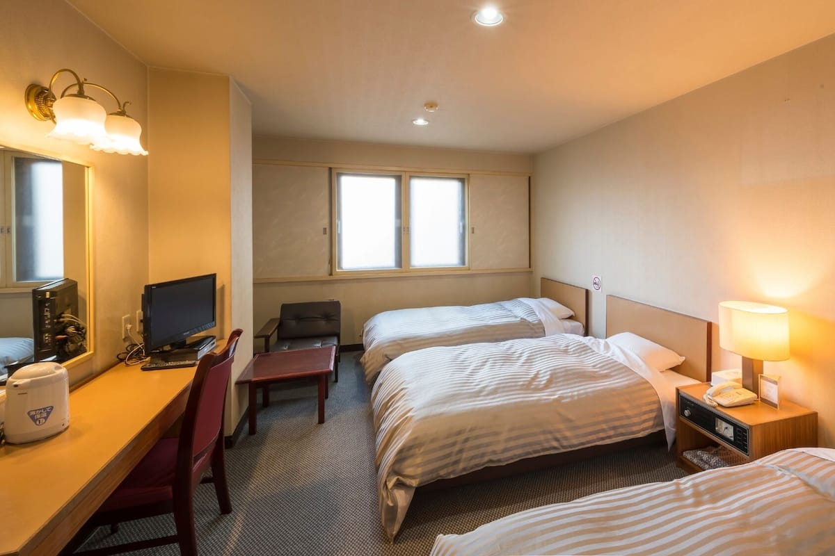 Habitación de hotel con dos camas, un escritorio con computadora, una silla, una lámpara de escritorio y una mesita de noche con teléfono.