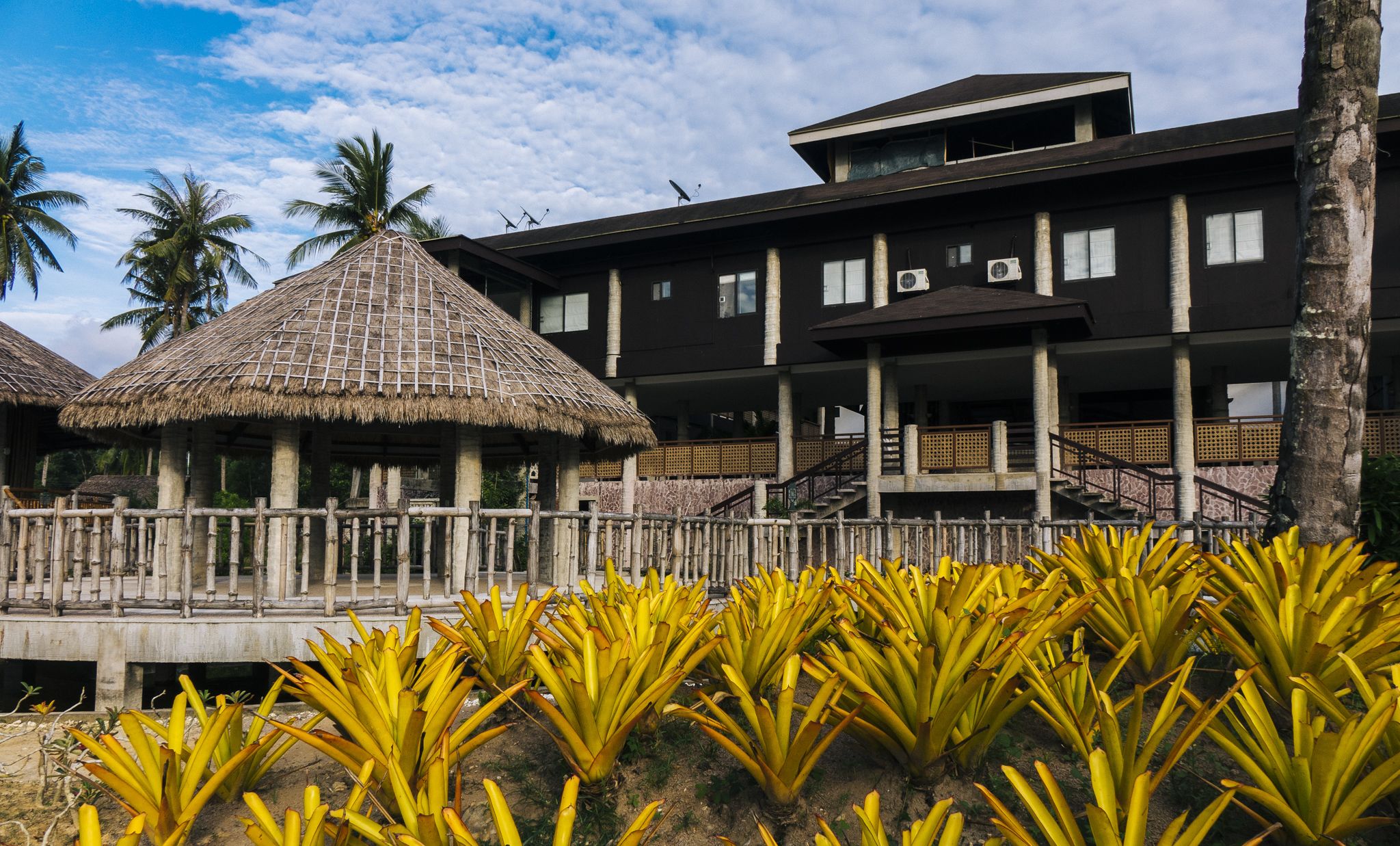 A resort with a thatched-roof structure, a modern building with multiple floors, and a staircase leading to the upper level.