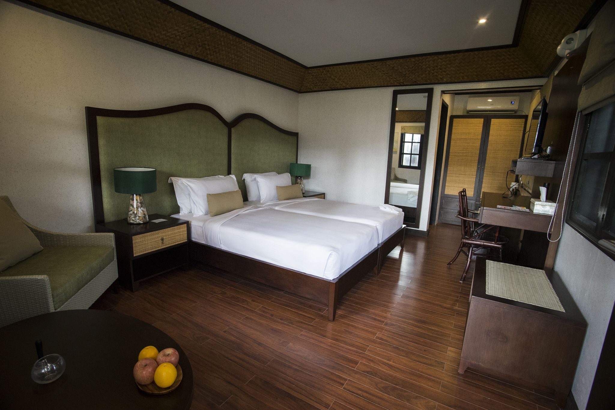 Habitación de hotel con una cama grande, un escritorio con silla, una mesita con fruta y un espejo.