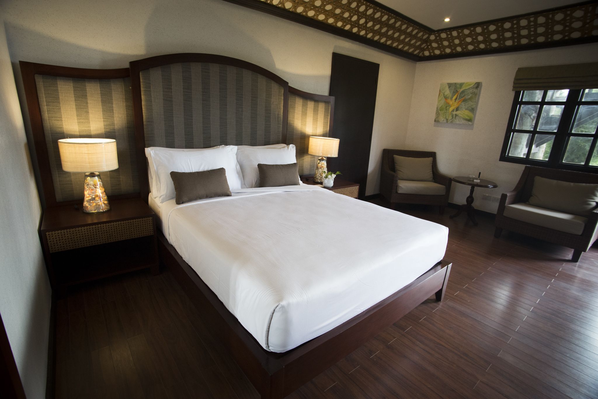A hotel room with a large bed, two bedside tables with lamps, a chair, a small table, and a window.