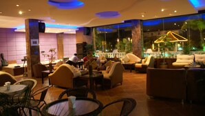 Un espacio interior bien iluminado con muebles modernos, incluyendo sofás y sillones, dispuestos alrededor de mesas. Hay ventanas amplias que ofrecen vistas al exterior.