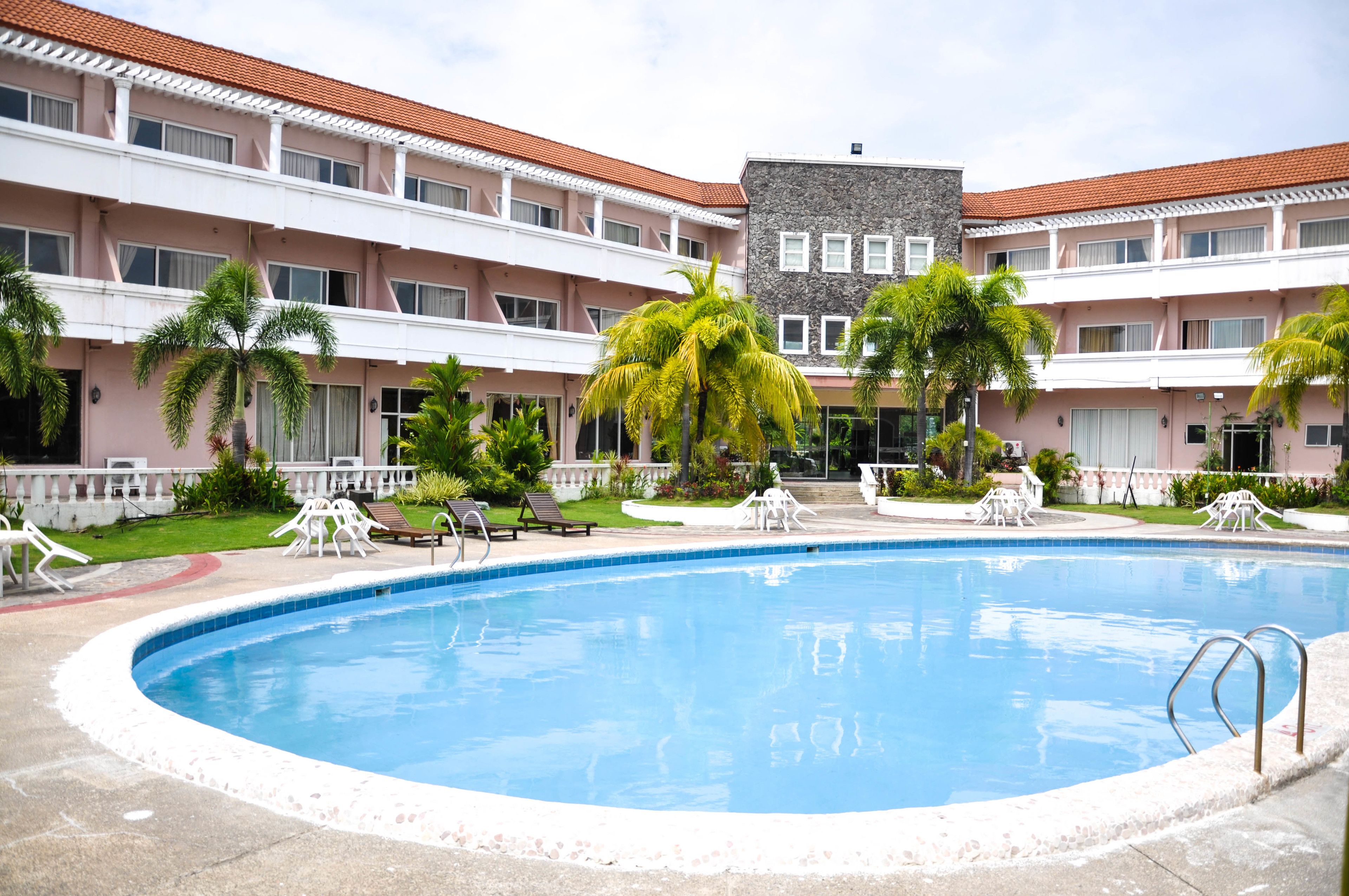 A swimming pool surrounded by palm trees and a building with a red-tiled roof.