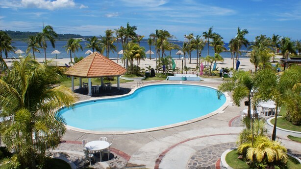 Una piscina con un pabellón, palmeras y vista al mar.