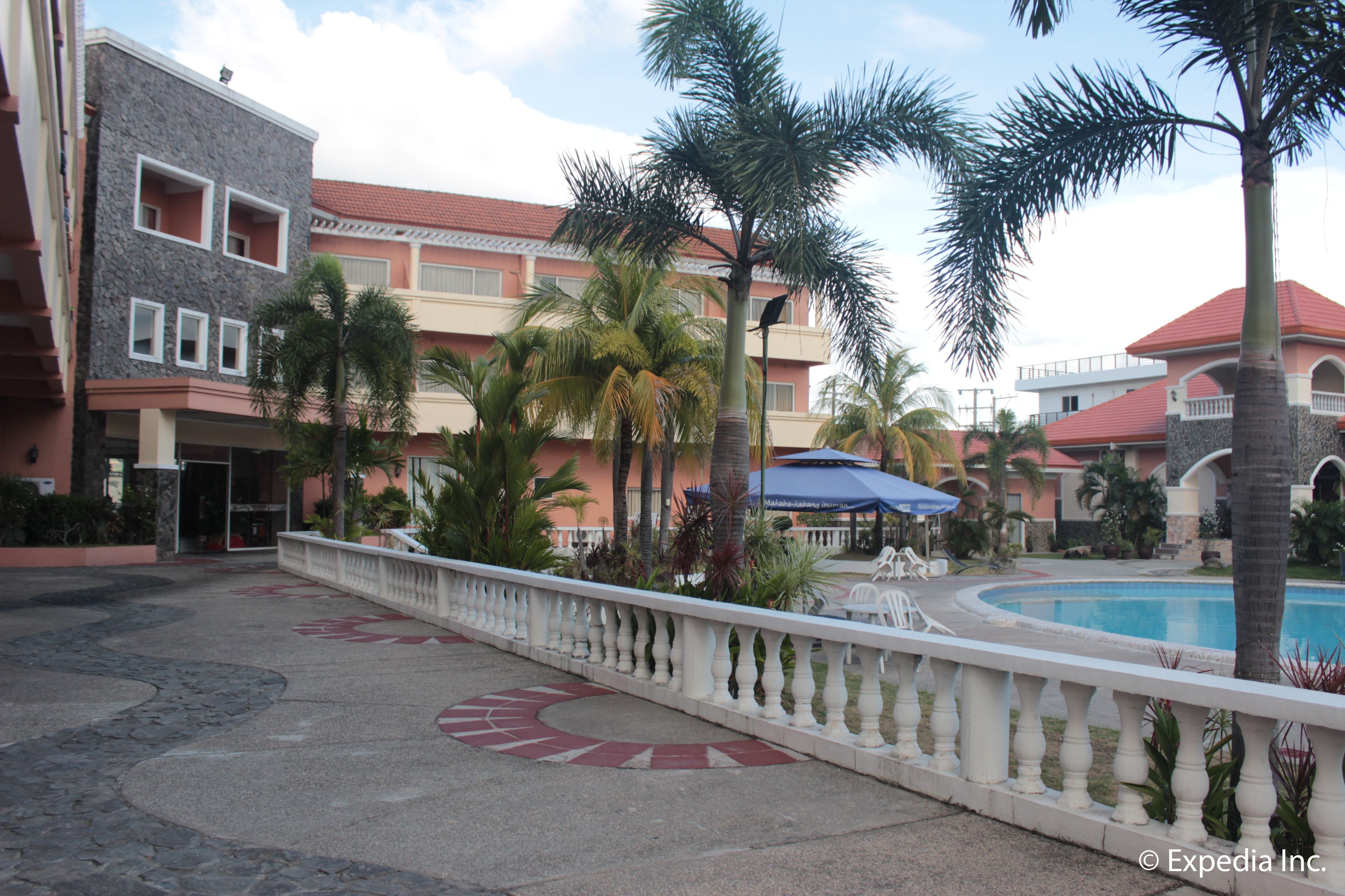 Un patio de hotel con piscina, palmeras y una barandilla blanca.